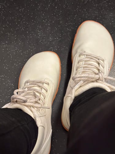 Asiakkaan jalassa vaaleat Vaistoa Hurmos Talvi 2 -paljasjalkamaiharit mustien housujen kanssa, ylhäältä kuvattuna.