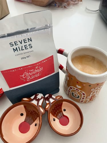 Customer's bag of The Christmas Blend coffee next to a festive gingerbread mug and two reindeer-shaped bowls.