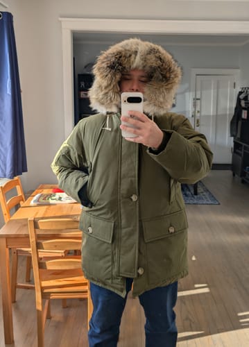 Reviewer wearing the olive Polar Down parka with the large fur hood up, taking a mirror selfie indoors.