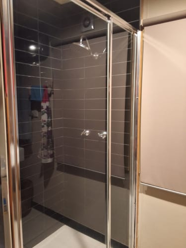 Customer's sparkling clean shower with a glass door and dark tiled walls, showing the results of the KoalaCloth.