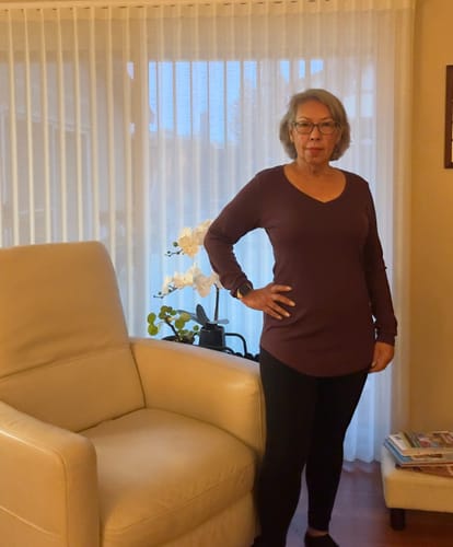 Reviewer standing in a living room wearing the long-sleeved Eva Tunic in Chocolate Plum with black leggings.