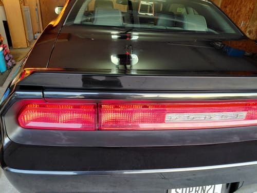 Reviewer's close-up of the shiny rear trunk and taillights of a detailed black Dodge Challenger.
