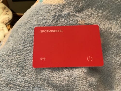 Reviewer's red SPOTMINDERS. Tracking Card resting on a soft blue textured surface.
