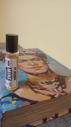 Recensore mostra il profumo ST INCENSE in formato roll-on, appoggiato su un libro artistico.