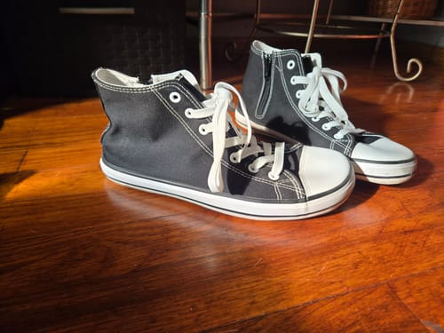 Reviewer's black high-top sneakers with a wide toe box and white laces sitting on a wood floor.