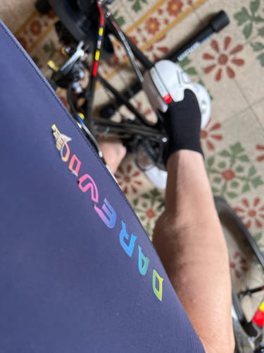 Close-up on the leg of a reviewer's blue bib shorts, showing the colorful 'DAREVIE' logo peeling off.
