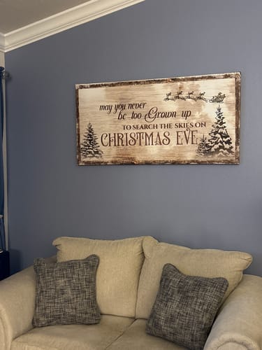 Customer's rustic Christmas Eve Farmhouse Sign hanging on a blue-grey wall above a sofa.