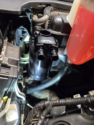 Customer's black billet oil catch can with dual ports installed in a car engine.