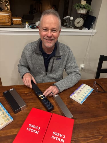 Customer's husband at a table with his new metal pill cases, transferring from an old plastic one.