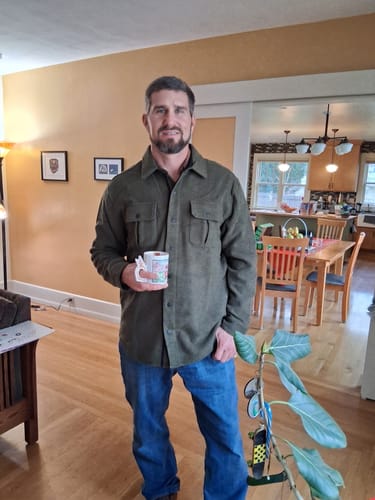 Reviewer standing indoors wearing the Wilder Shirt Jac in Dark Forest as a comfortable, casual jacket.