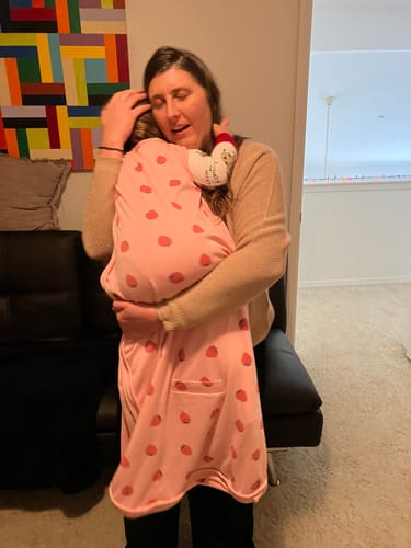 A reviewer hugs a toddler wearing the pink strawberry-print 4 Season Ultimate Baby Sleep Bag.