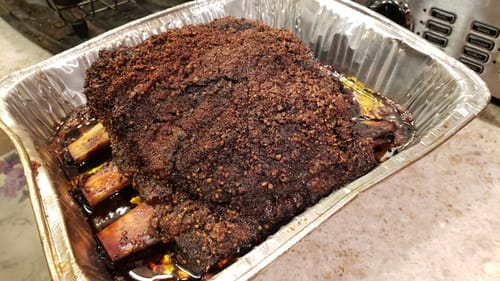 Reviewer's smoked Bone-In Short Ribs with a dark crust, resting in a foil pan.