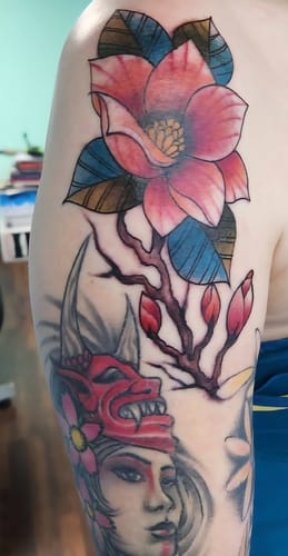 Customer's upper arm showing a colorful new tattoo of a magnolia flower, applied using the numbing cream.