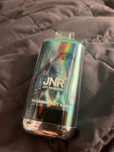 Customer's JNR Falcon X 18000 Puffs Disposable Vape in the Passion Fruit Kiwi flavor, resting on a dark comforter.
