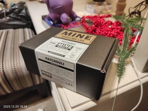 Recensore mostra la scatola del profumo PATCHOULI su un mobile, con decorazioni natalizie sullo sfondo.