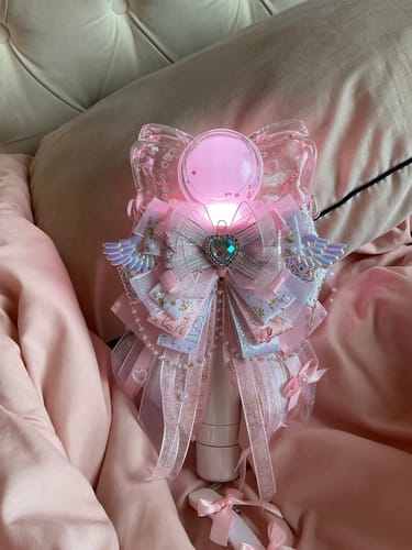 Customer's decorated IZNA OFFICIAL LIGHT STICK, glowing with a pink light while resting on a bed.