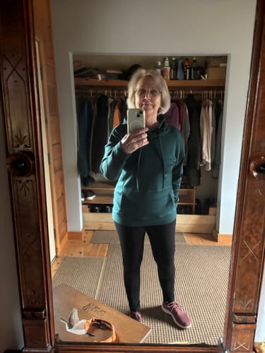 Reviewer taking a mirror selfie to show the fit of the green Callie Hoodie with black leggings.