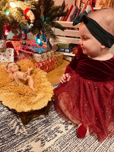 A customer wearing the red Velour Ballerina Dress with a velvet top and sparkly tulle skirt by a Christmas tree.