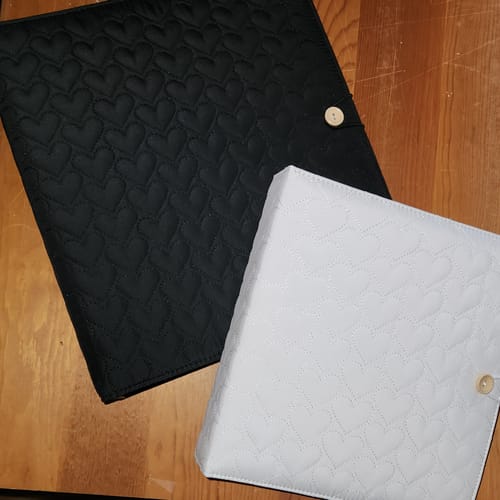 Customer's black and white Cupid's Collection binders with quilted heart patterns on a wooden table.