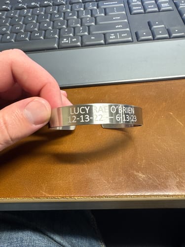 Customer holding their customized stainless steel cuff bracelet with an engraved name and dates.