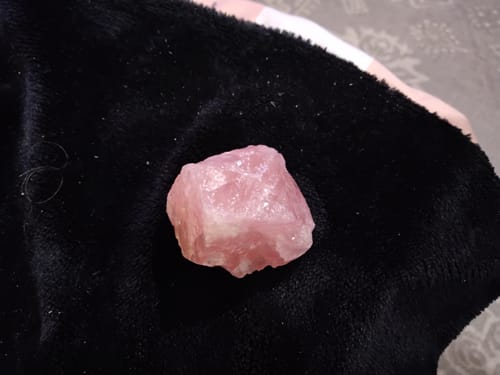 A reviewer's rough rose quartz crystal shown up-close on a soft black fabric.