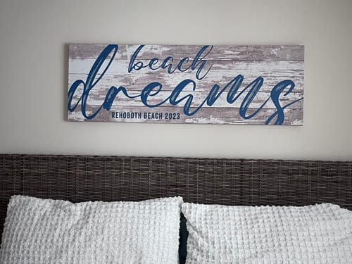 Customer's personalized Beach Dreams Sign with blue script hanging on a wall above a bed in a guest room.