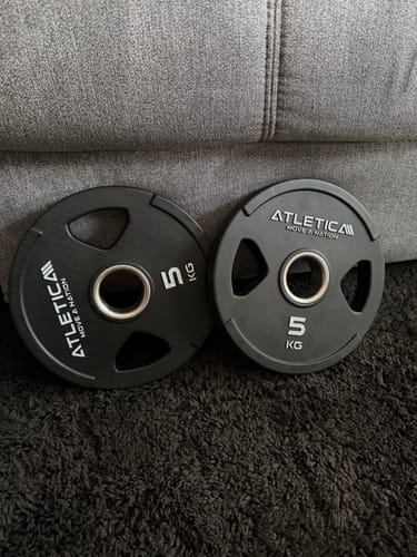 Rezensent zeigt ein Paar der 5-kg-2H-Gripper-Hantelscheiben, die auf einem dunklen Teppich liegen.