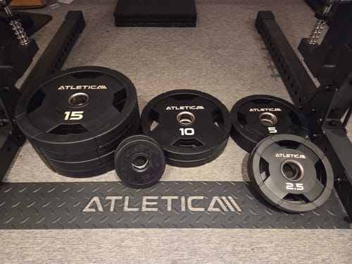 Ein Kunde zeigt seine schwarzen 4H Gripper Hantelscheiben von 2,5 kg bis 15 kg, die auf einem Fitnessboden liegen.