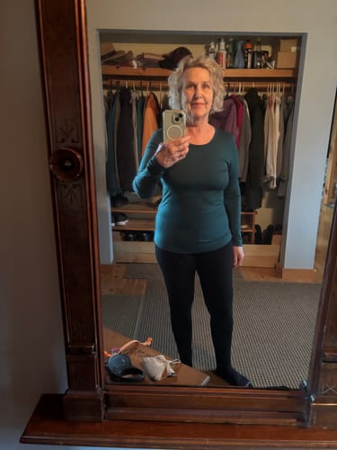 Reviewer in a bedroom wearing the slim-fitting Remi Long Sleeve T-Shirt in Riverbank Green with black leggings.