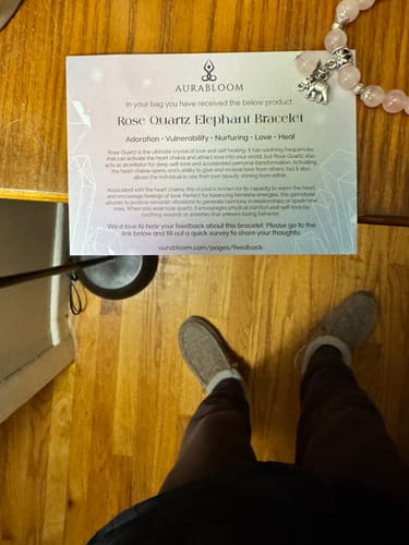 Reviewer's Rose Quartz Elephant Bracelet and its description card laid out on a wooden surface.