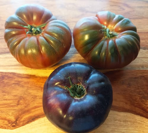 Kundenbild von drei großen, reifen Tomaten aus dem Tomatenmix von Julian auf einer Holzoberfläche.
