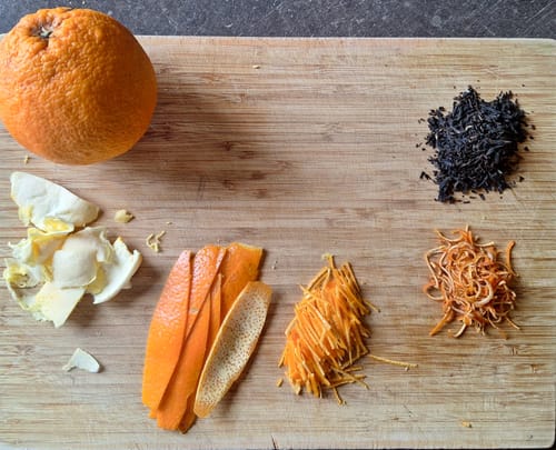 Rezensent zeigt vorbereitete Schalen der Bio Navel Orange und schwarzen Tee auf einem Holzbrett.