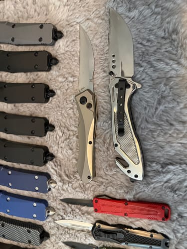 Customer's Hendrix Hell Hawk switchblade shown open among a collection of other automatic knives on a fuzzy surface.