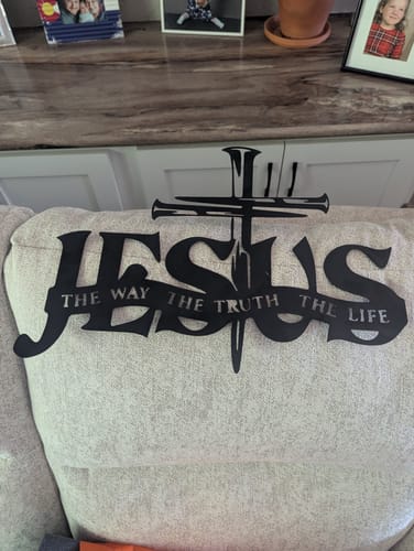 Customer's black Jesus & Cross metal wall decor resting on a light-colored sofa.