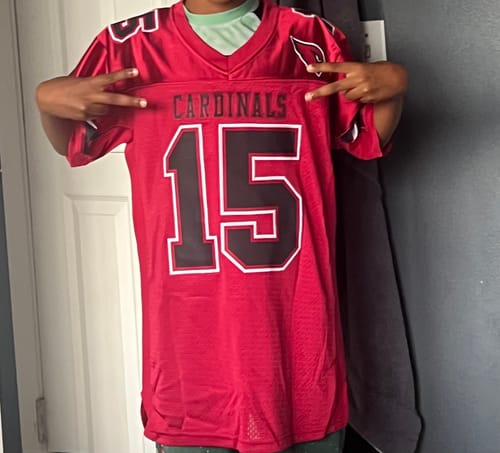 Customer making peace signs while holding a red Cardinal football jersey with the number 15.