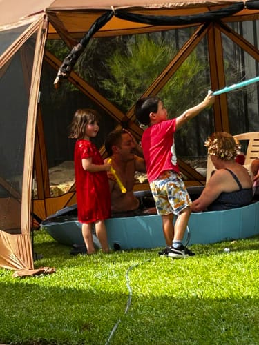 Reviewer's family cooling off in the blue foldable Pet Dog Pool on a grassy lawn.