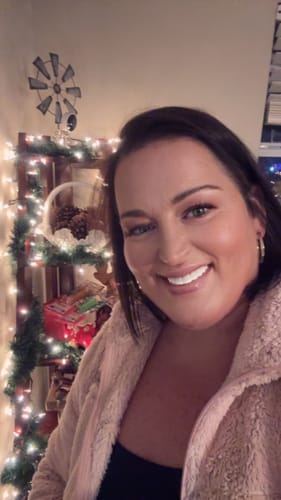 Customer smiling happily and showing off her bright white Pop On Veneers in front of a festive background.