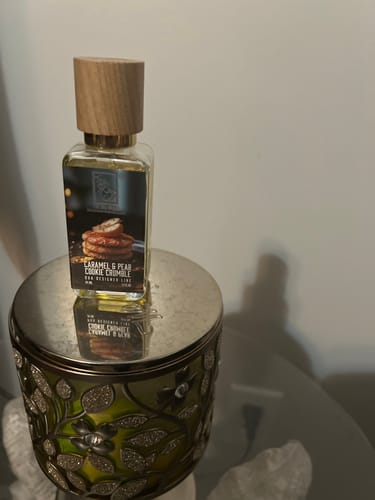 Reviewer's Caramel & Pear Cookie Crumble perfume bottle with a wood cap, sitting on a decorative silver and green holder.
