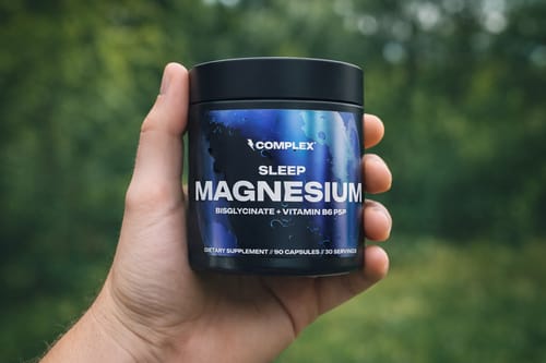 Customer holding the black tub of Complex Sleep Magnesium supplement against an outdoor background.