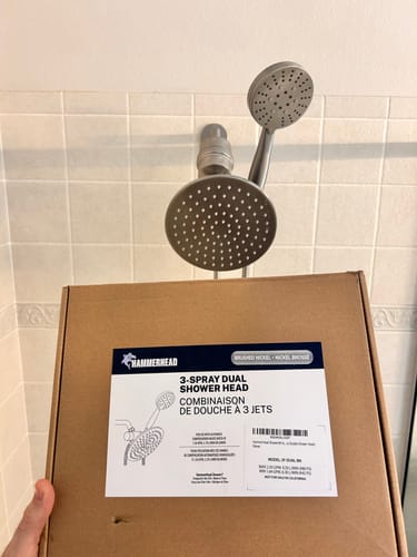 Customer holds the box for the 3-Spray Dual Shower Head Set with the product installed in their shower.