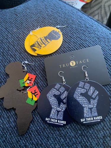 Reviewer displays their yellow Black lives Matter wooden earring alongside two other pairs of earrings mentioned in the review.