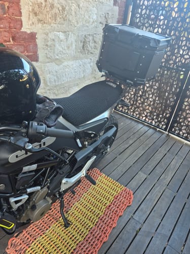 Customer's black Wind Rider Seat Cover fitted onto a motorcycle parked on a wooden deck.