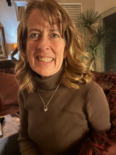 Customer's wife smiling while wearing the silver-toned Forever Love Necklace over her brown turtleneck sweater.