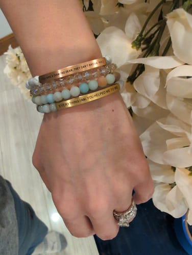 Reviewer wearing a stack of bracelets, including the gold-tone "EVERYTHING I AM YOU HELPED ME TO BE" beaded bracelet.