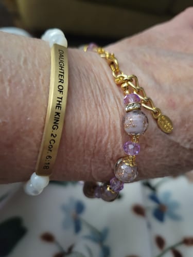 Close-up of a customer's wrist wearing the gold-colored DAUGHTER OF THE KING cuff bracelet with a beaded one.