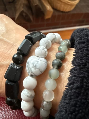 Customer's wrist wearing a white Howlite crystal bracelet with a heart-shaped bead, stacked with two other bracelets.
