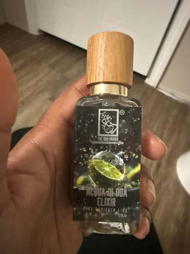 Customer holding a bottle of Acqua Di Dua Elixir, showing the clear bottle, wooden cap, and dark label with a lime graphic.