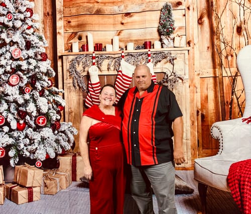 Customer wearing the red velvet jumpsuit while posing for a festive holiday photo with a companion.