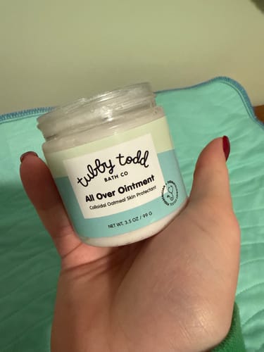 Customer holding an open jar of the white Tubby Todd All Over Ointment.