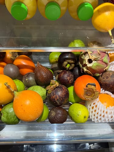 Rezensent zeigt die bunte Vielfalt der Weihnachts-Danke Box mit Kaki, Mangostan und Passionsfrucht in einem Kühlschrankfach.
